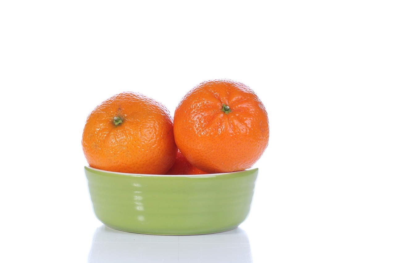 Two oranges sit in a glossy light green ceramic bowl against a bright white background.