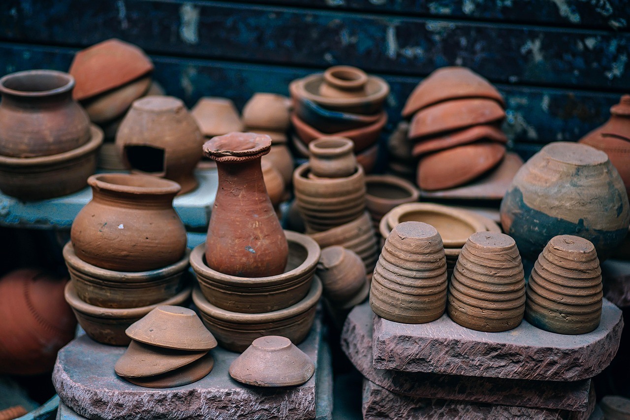 Many unglazed earthenware pots, bowls, lids, and stacked cups are displayed on rustic stands.